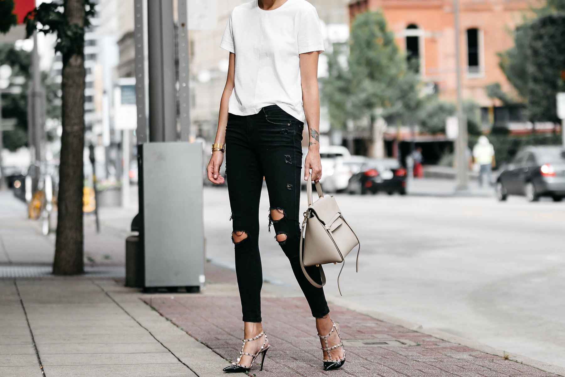 Woman, wearing white t-shirt, black shorts, fanny pack or waist pack and  bucket hat, standing outdoor near white wall. Details of stylish trendy  basic minimalistic casual outfit. Street fashion. Photos