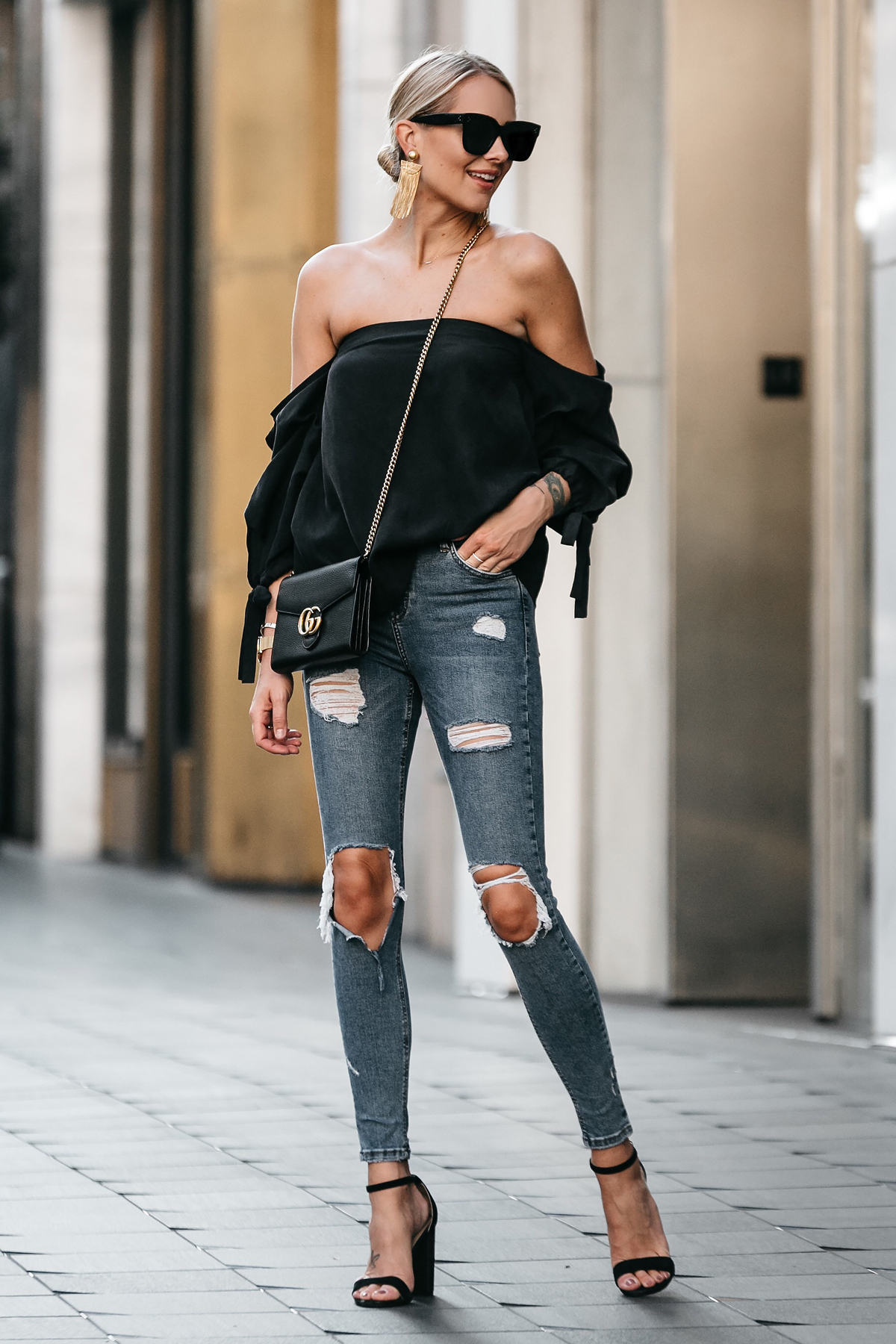 Blonde Woman Wearing Club Monaco Black Off-the-Shoulder Top Denim Ripped Skinny Jeans Outfit Black Ankle Strap Heels Gucci Marmont Handbag