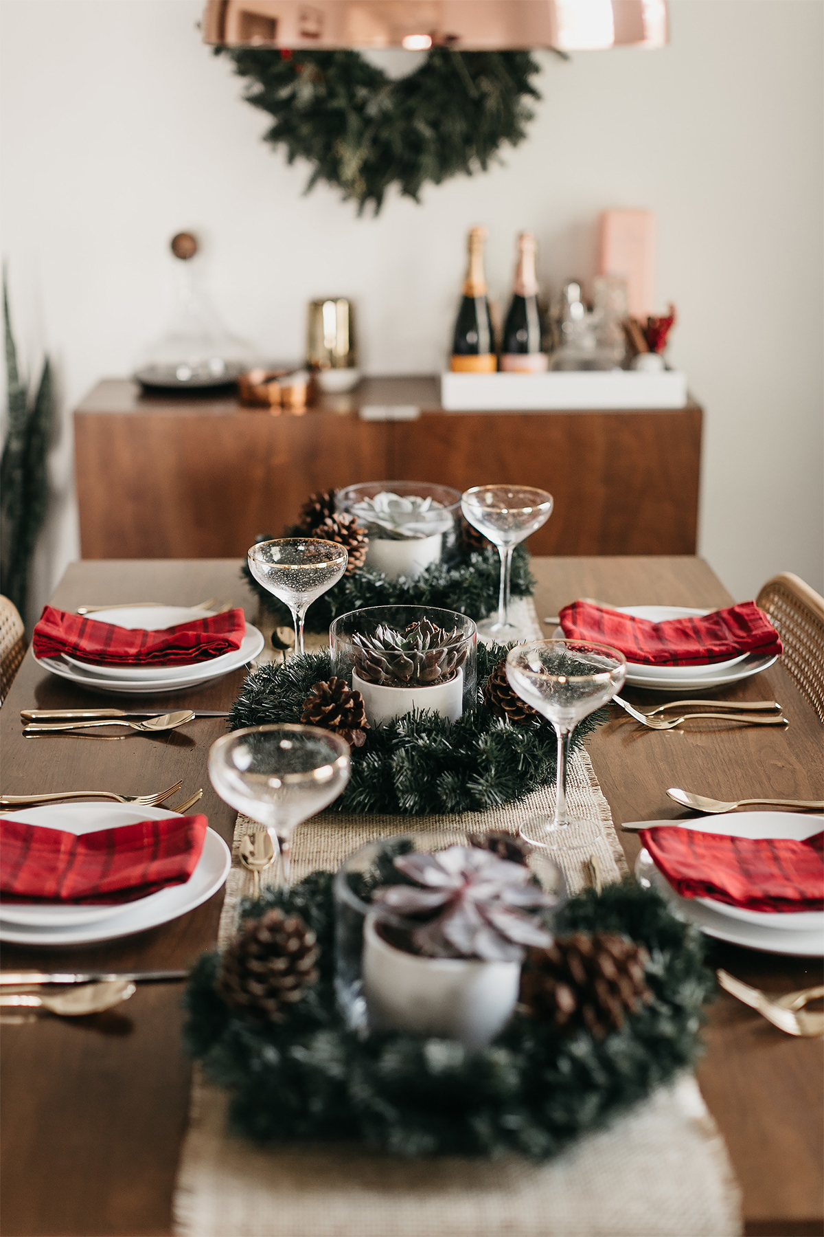 Mode Jackson Noël Tablescape Plaid Rouge Serviettes Vaisselle Blanche Couverts Or Flûtes à Champagne Or Couronne Cône Pin Centre De Table 1