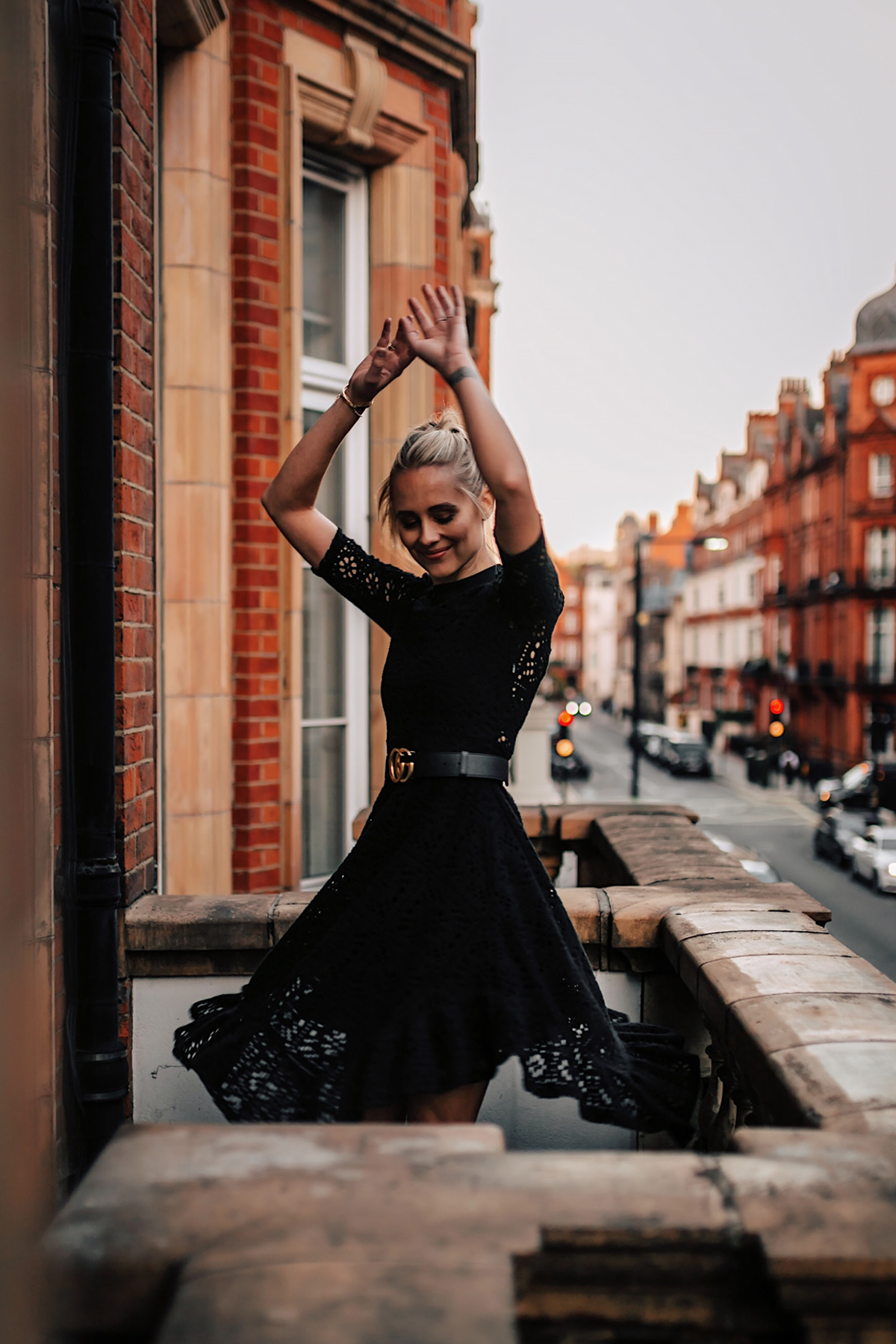 Blonde Women Twirling Wearing Black Lace Dress with Gucci Belt on London Balcony