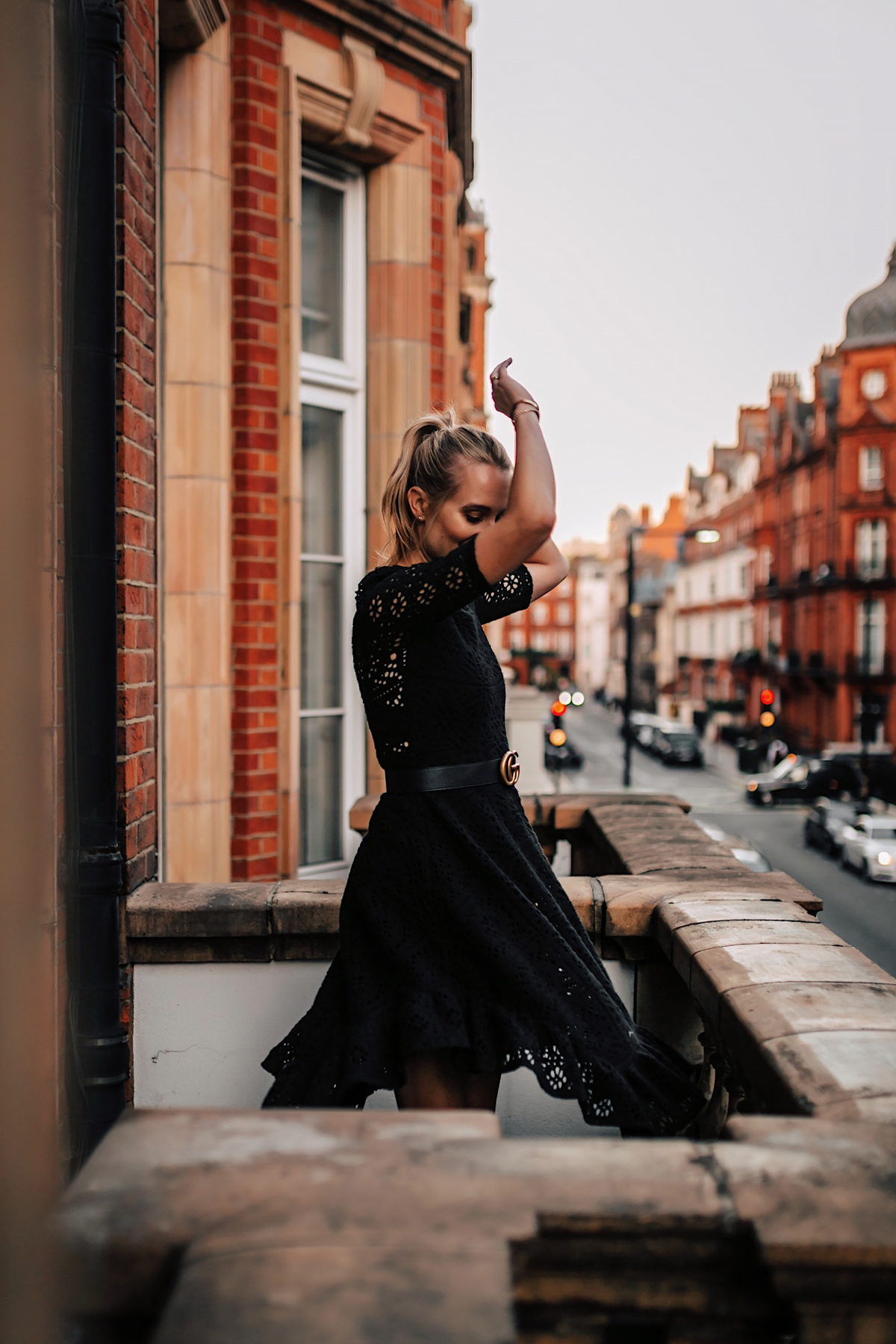 Blonde Women Twirling Wearing Black Lace Dress with Gucci Belt on London Balcony