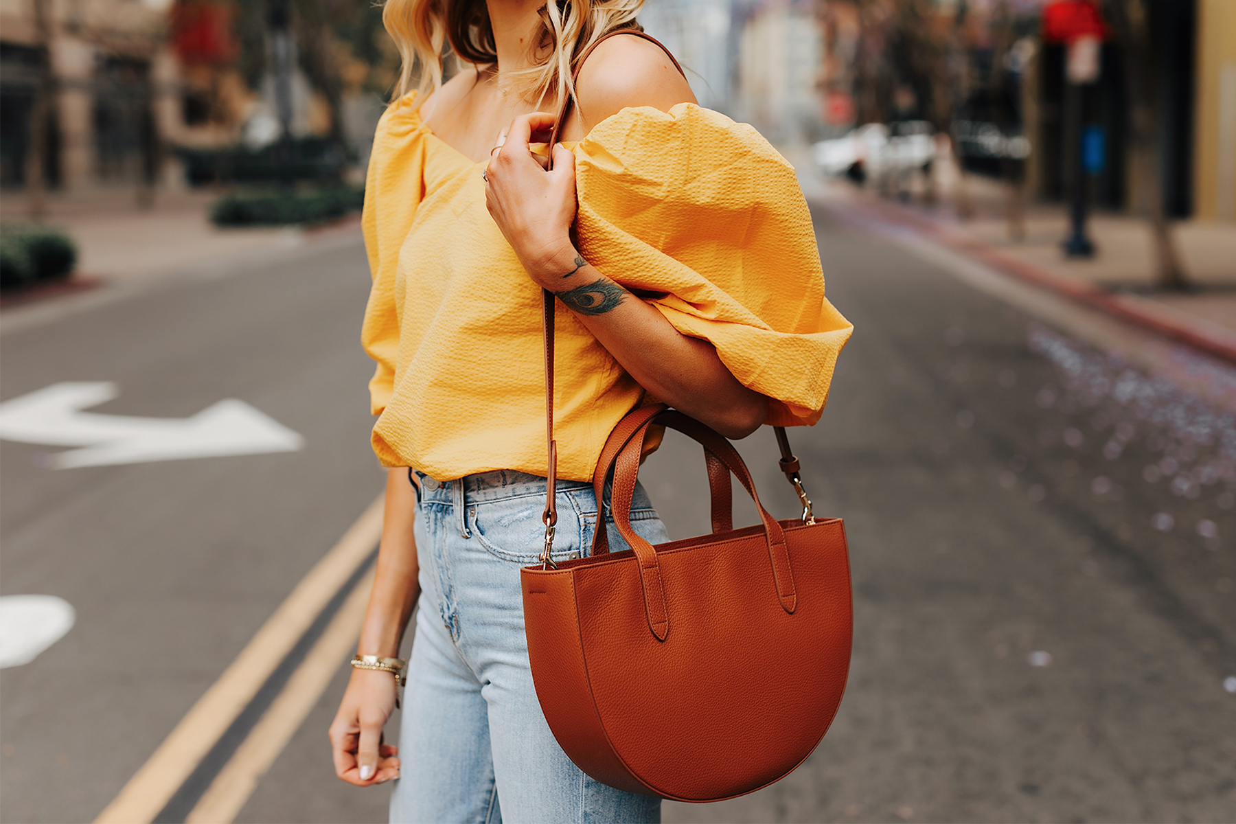 Fashion Jackson Wearing Cuyana Yellow Off the Shoulder Blouse Light Wash Jeans Cuyana Tan Semi Circle Handbag