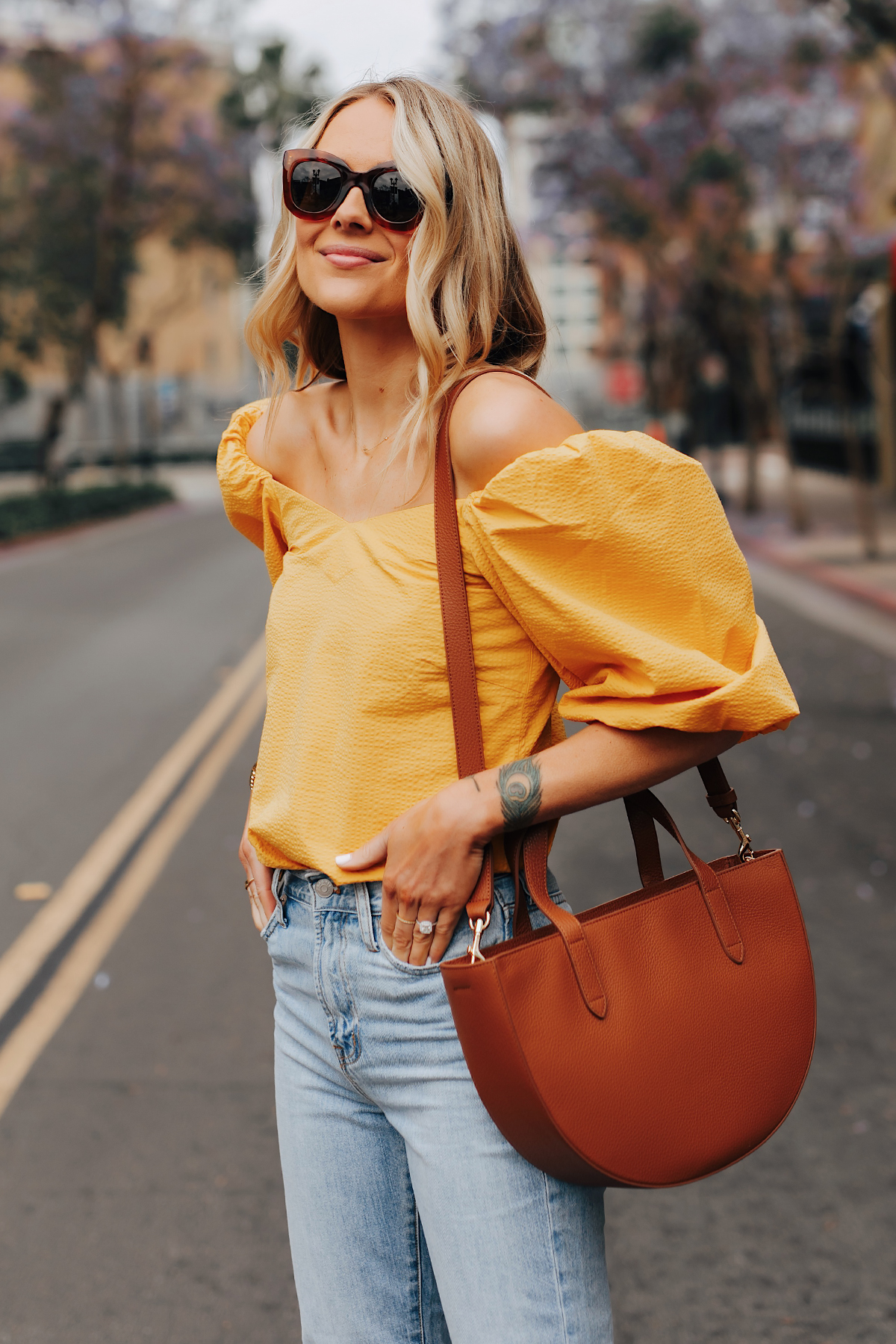 Fashion Jackson Wearing Cuyana Yellow Off the Shoulder Top Light Wash Jeans Cuyana Tan Semi Circle Handbag