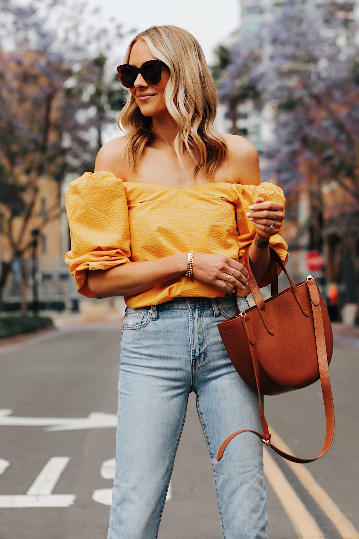 Fashion Jackson Wearing Cuyana Yellow Off the Shoulder Top Light Wash Jeans Cuyana Tan Semi Circle Handbag