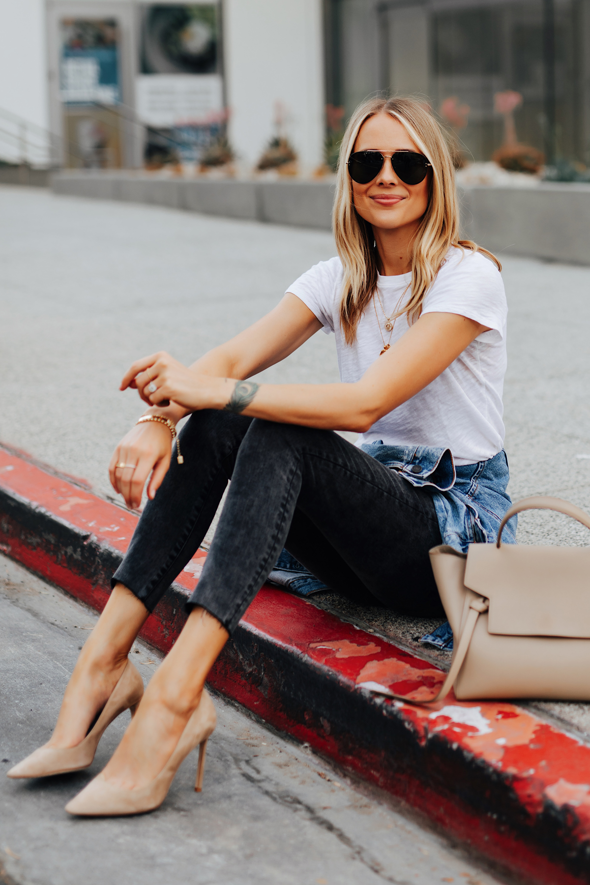 Young beautiful woman, wearing beige t-shirt, black pants, bucket hat and gold  chain necklace, standing outdoor near white roller door. Stylish trendy  basic minimalistic casual outfit. Street fashion. Stock Photo