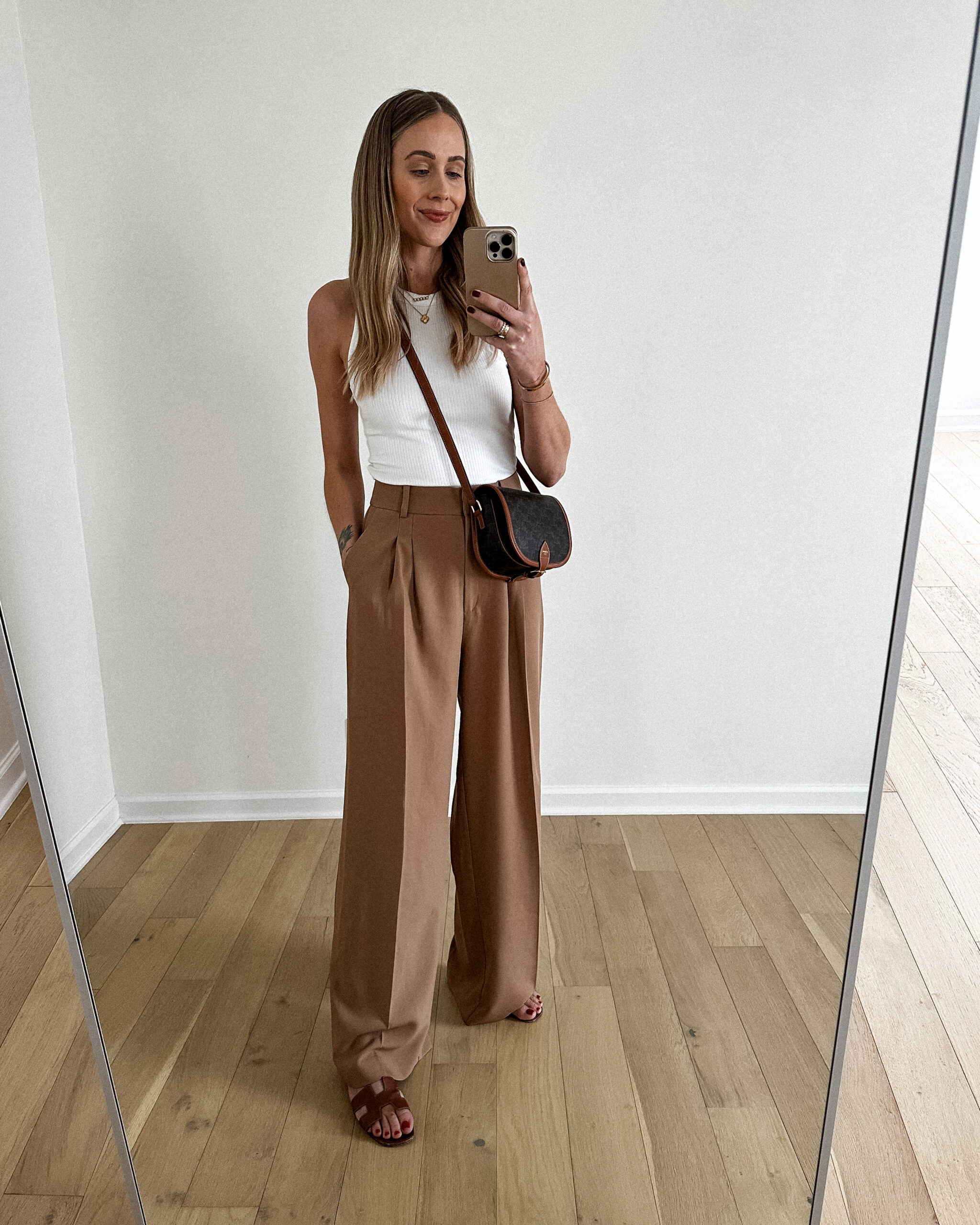 Fashion Jackson wearing MAYSON the label white rib fitted tank, tan trouser pants, heremes oran gold sandals, celine logo crossbody handbag, casual outfit